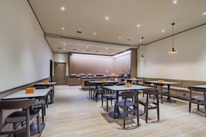 En modern restaurang med flera bord och stolar, ett köksområde och hängande lampor.