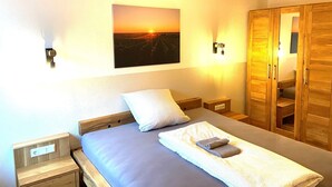 A bedroom with a bed, a nightstand, a wall-mounted picture, and a wooden wardrobe.