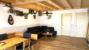 A cozy room with a wooden ceiling, a black sofa, a wooden dining table with chairs, and a small round table with a plant.