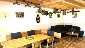 A modern dining area with a wooden table and chairs, a black sofa, and a small round table with a plant.