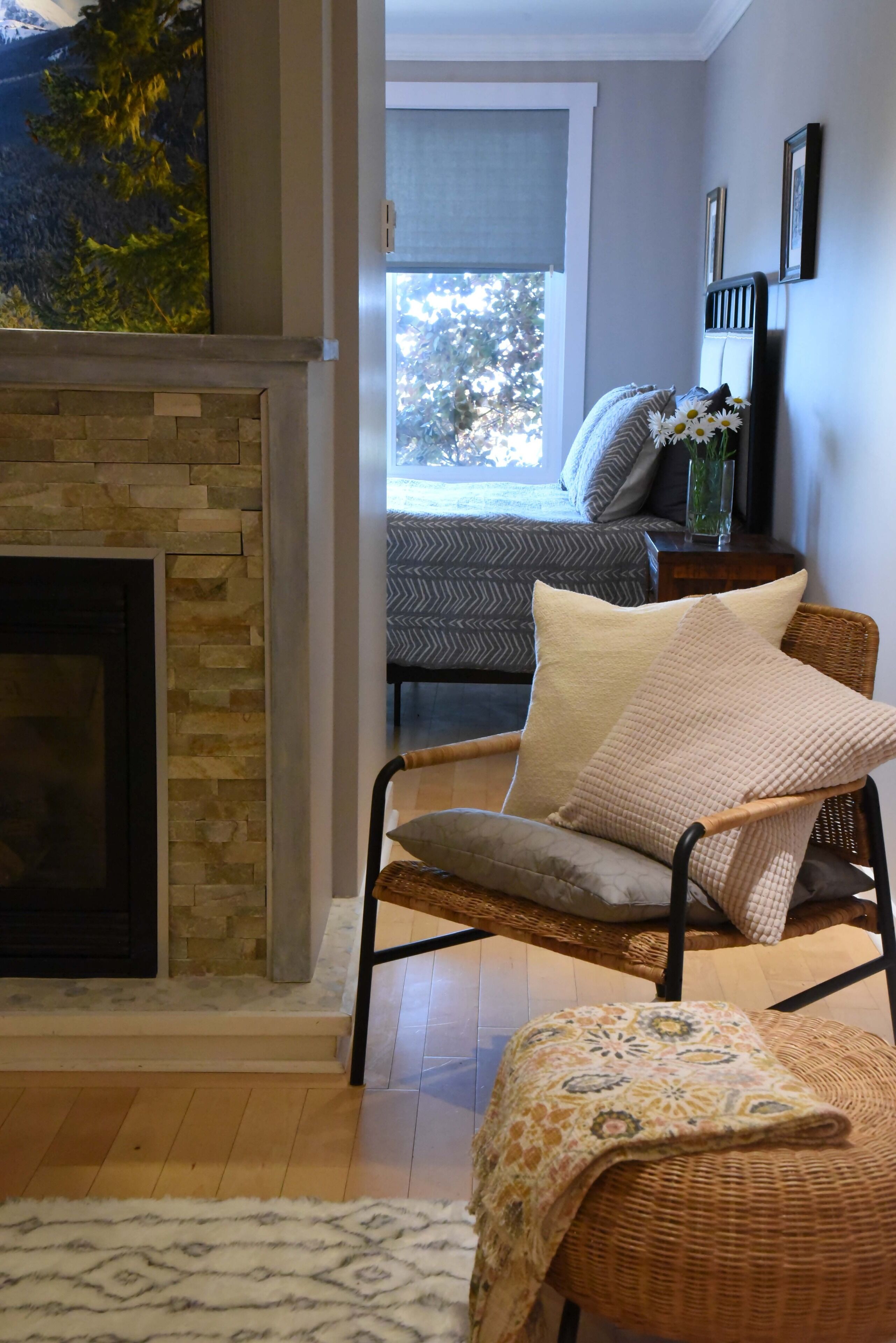 A living room with a stone fireplace, wicker furniture, a patterned rug, and a view of the outdoors through a window.