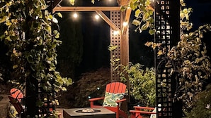 An outdoor patio area with a wooden pergola, red Adirondack chairs, and a fire pit.