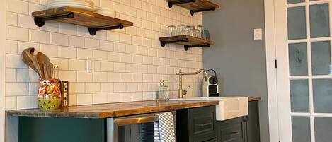 Una cocina con azulejos blancos tipo metro, estantes de madera, un refrigerador de acero inoxidable y un ventanal con vidrio esmerilado.