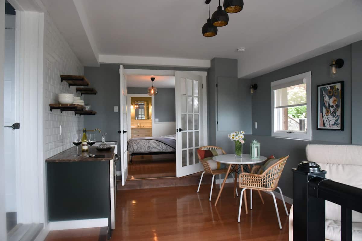 A modern kitchen with wooden shelves, a dining area with wicker chairs, and a cozy living space with a sofa and a fireplace.