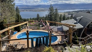 A wooden deck with a swimming pool, surrounded by a wooden fence, overlooking a lake and distant mountains.