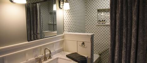 A bathroom with a sink, mirror, and shower.