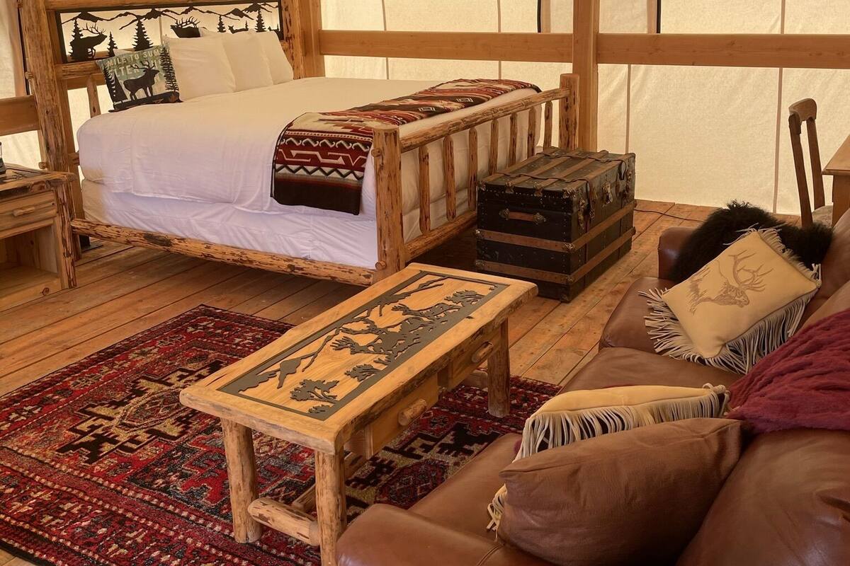 A tented accommodation with a bed, a wooden bench, a leather couch, and a patterned rug.
