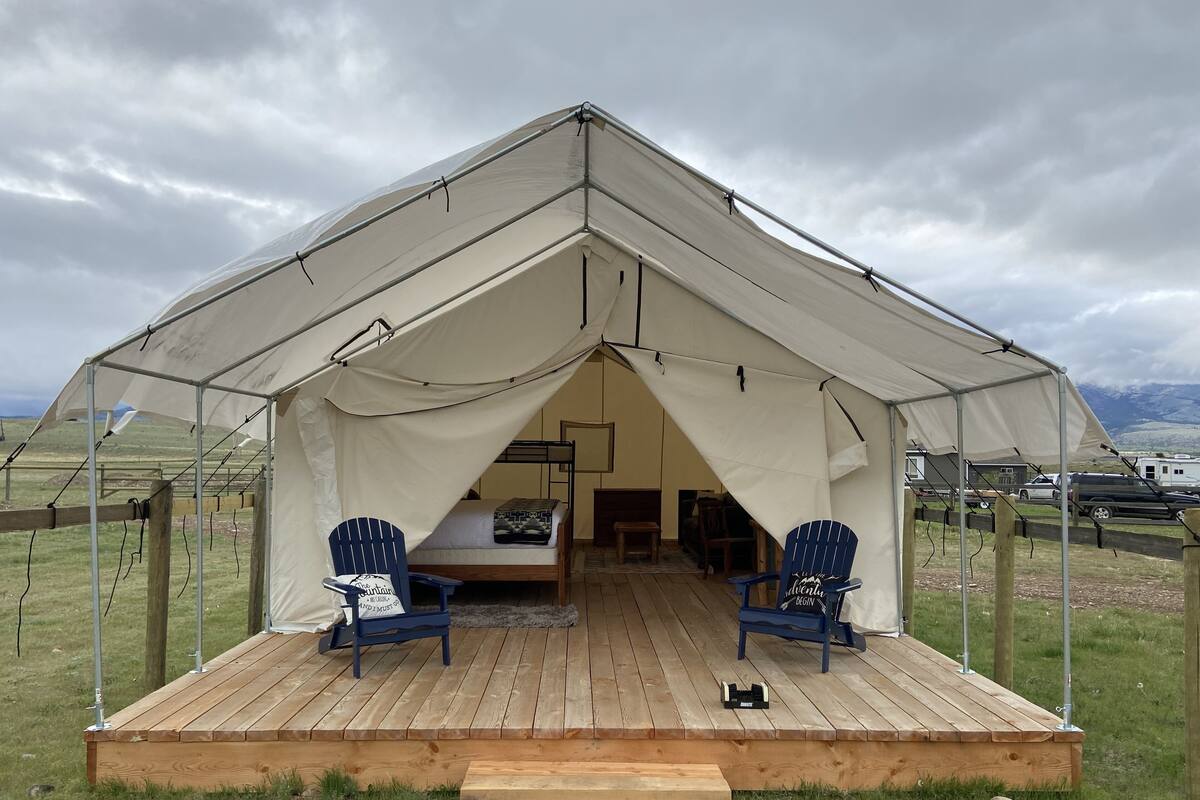 A tent with a wooden deck, two blue chairs, and a bench.