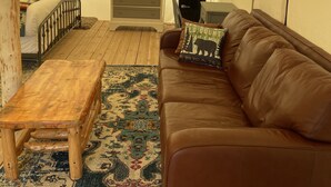 A tented room with a wooden bench, a brown leather couch, a patterned rug, and a small table. - Yellowstone Dreamin Camp (Pray)