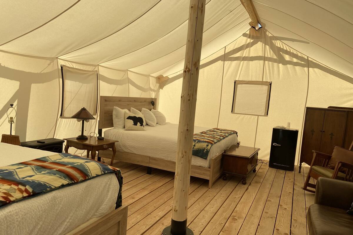 A tented accommodation with a large bed, a smaller bed, a desk, a chair, and a wardrobe.