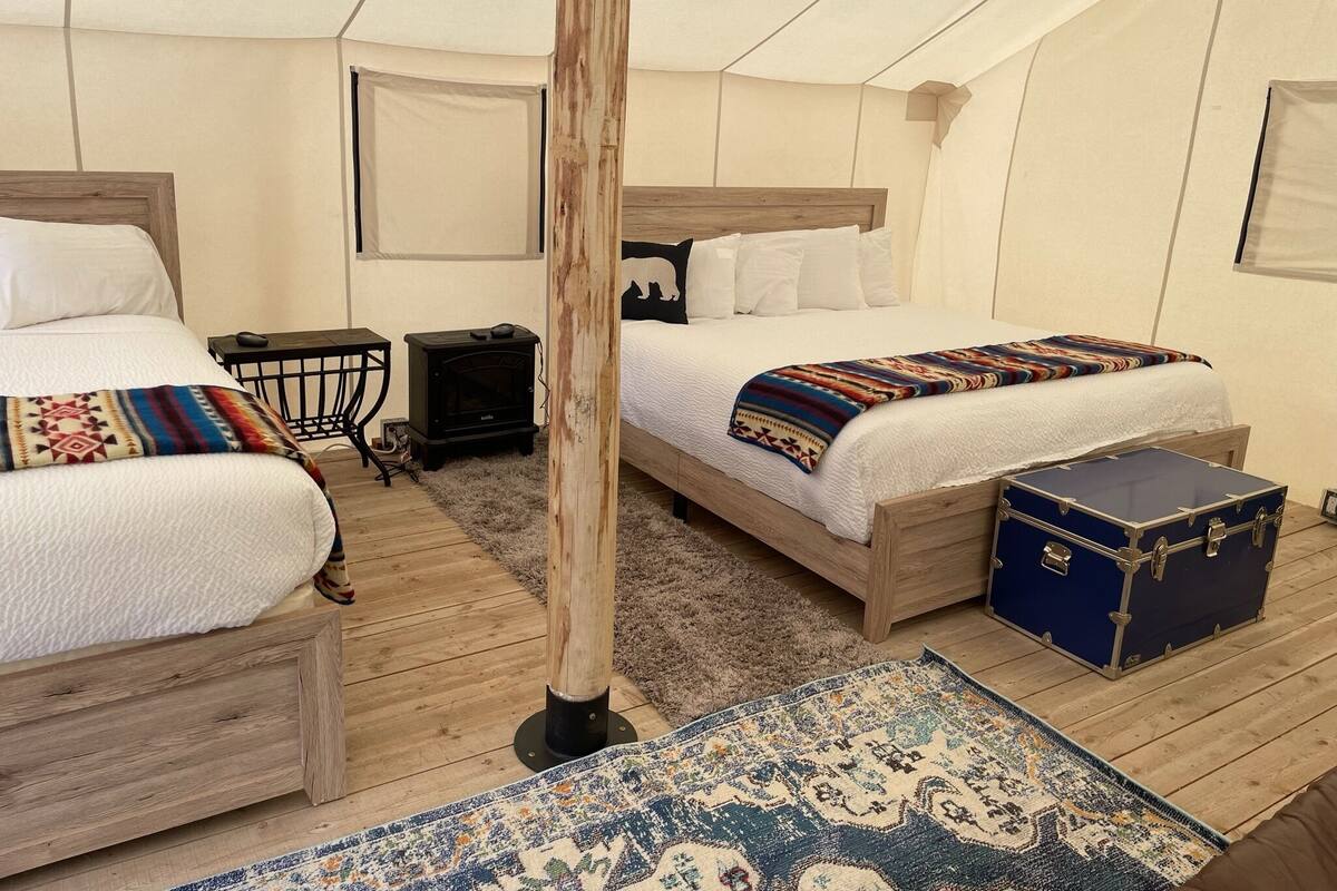 A tented room with two beds, a heater, a suitcase, and a patterned rug.
