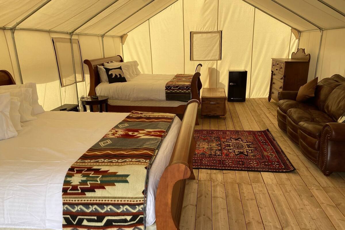 A tented accommodation with two beds, a wooden floor, a leather sofa, and a patterned rug.
