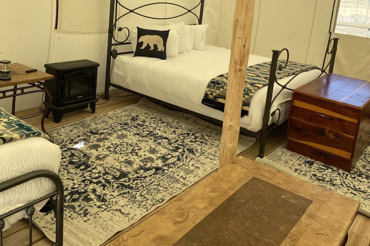 A tented room with a bed, a heater, a wooden chest, and a rug.