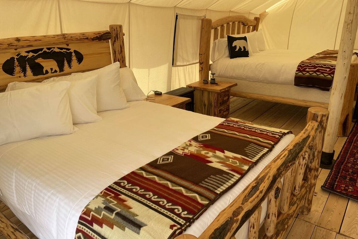 A tented accommodation with a large bed, a smaller bed, and a wooden headboard with a bear design.