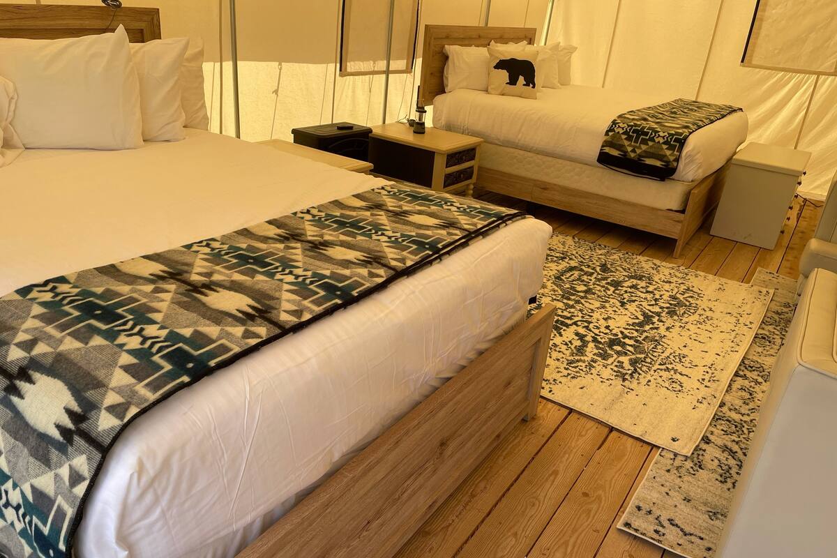 A bedroom with two beds, a wooden headboard, a patterned throw blanket, and a rug.