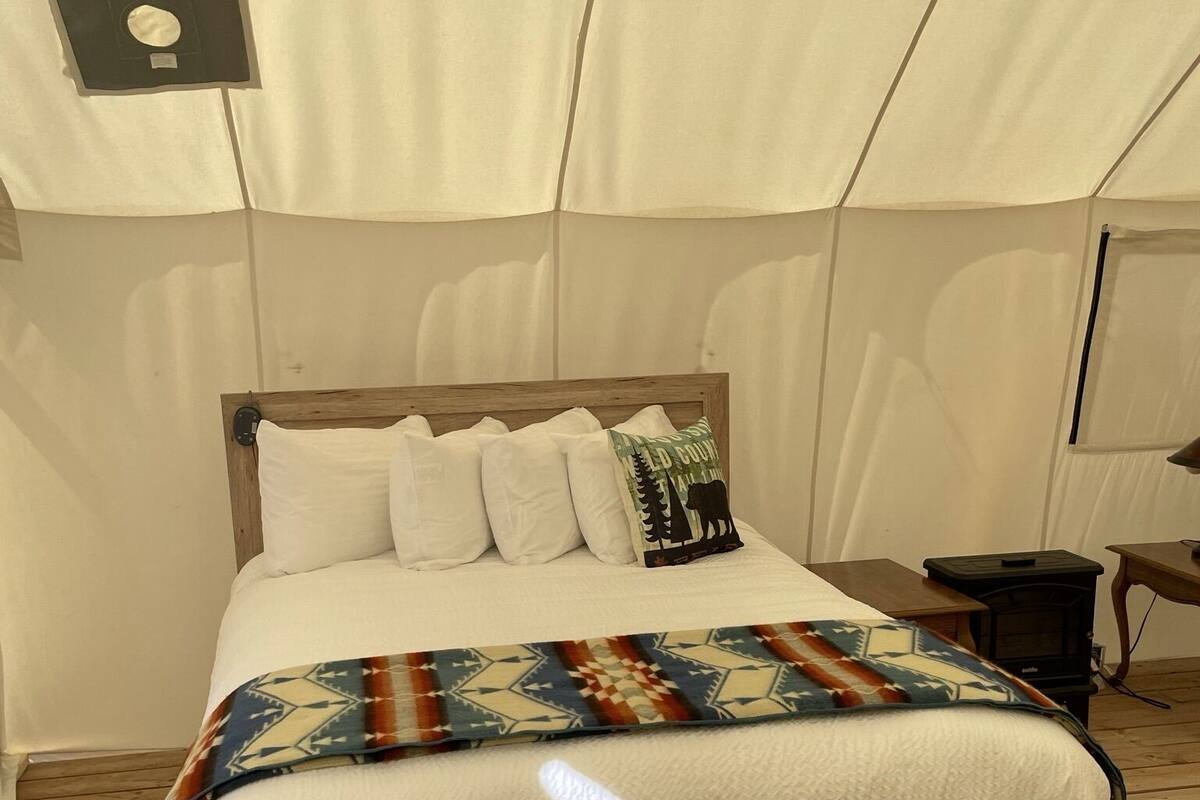 A bed with a wooden frame and white bedding, a patterned throw blanket, and a pillow with a forest design.