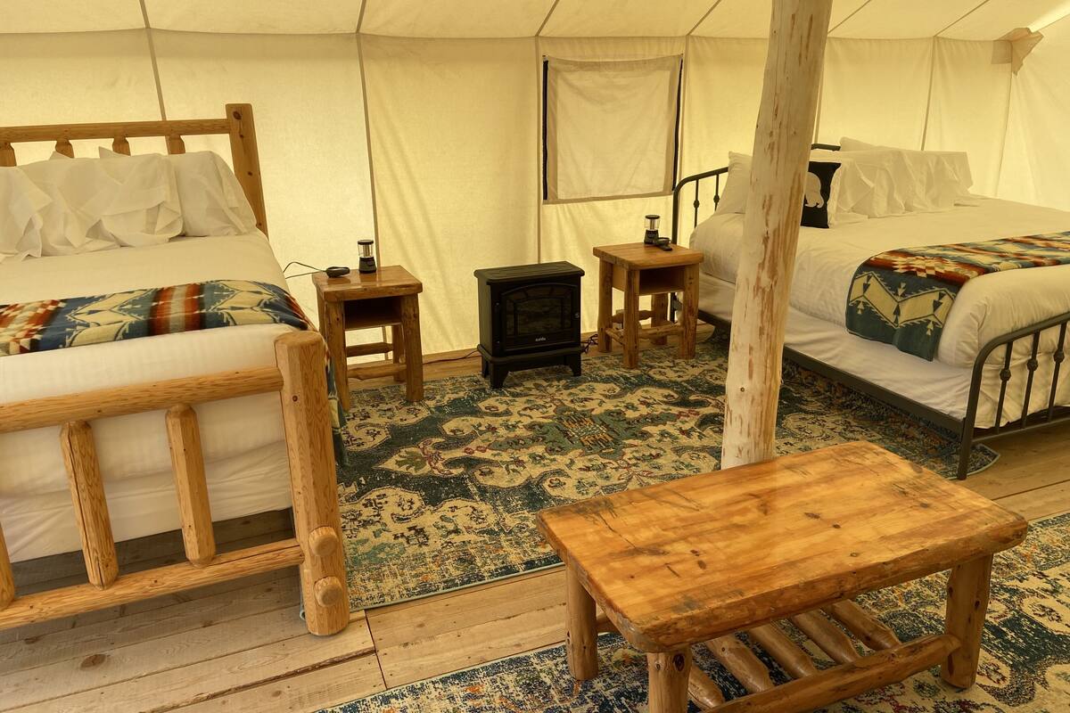 A tented accommodation with two wooden beds, a small wooden table, a stove, and a patterned rug.