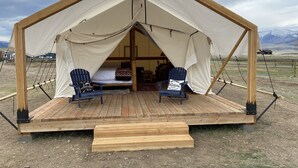 A wooden tent with a platform and two chairs, one with a cushion that says "The Mountains Call." - Yellowstone Dreamin Camp (Pray)