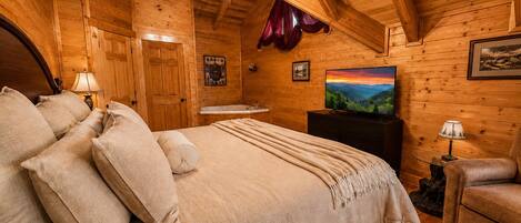 A wooden cabin bedroom with a bed, a television, a desk, and a chair.