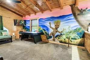 A room with a pool table, a green couch, and a mural of a character.