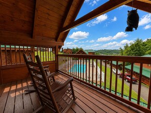Eine Holzterrasse mit Schaukelstuhl, Pool und Blick auf Häuser und Grünflächen.