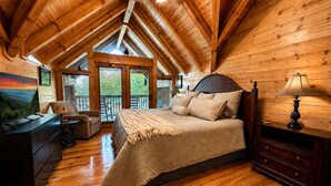 A log cabin bedroom with a bed, dresser, and a TV displaying a scenic view. - Groot's Place - 5min from parkway - massage chair/pool table/foosball (Pigeon Forge)