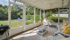 Eine überdachte Terrasse mit Korbmöbeln, einem Grill und Blick auf einen Garten.