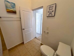 A bathroom with a toilet, a sink, and a shower. There is a door leading to another room.