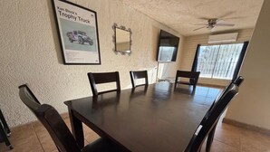 Ett konferensrum med ett stort bord och sex stolar, en takfläkt och ett fönster med galler.