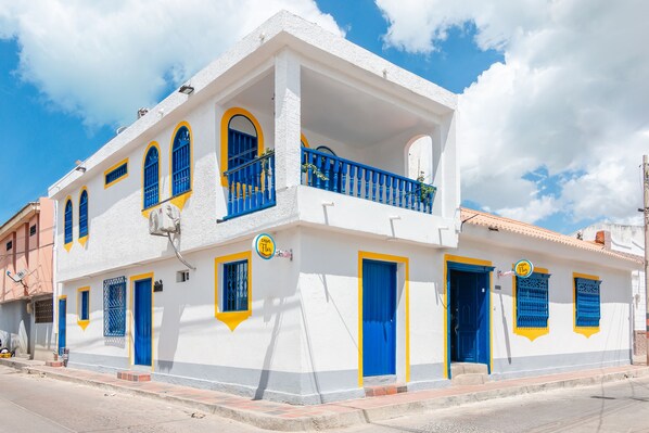 Un edificio blanco con puertas y ventanas azules, un balcón y un letrero que dice 'Casa Flor'.