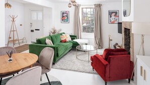 Een moderne woonkamer met een groene bank, een rode fauteuil en een glazen salontafel. Er is een kapstok en een eettafel met stoelen.