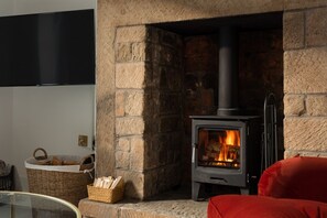 A stone fireplace with a modern wood-burning stove, a basket of firewood, and a red chair. - ✨ Stylish Grade II Listed Cottage in the Heart of Alnwick (Northumberland)