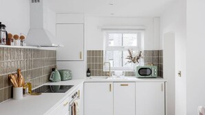 Een moderne keuken met witte kastjes, een groene magnetron en een raam boven de gootsteen.