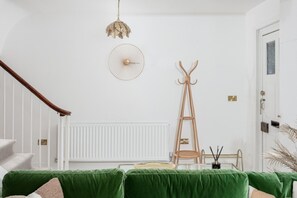 A room with a staircase, a coat rack, a fan, and a green upholstered sofa.