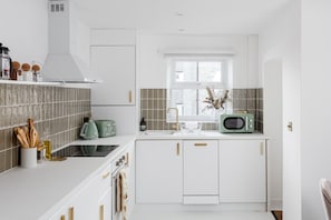 Una cucina moderna con mobili bianchi, una cappa aspirante in acciaio inossidabile, una finestra con vista e un forno a microonde in stile vintage.
