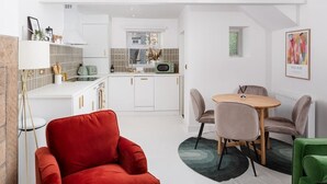 Een moderne keuken met witte kasten, een eethoek met een ronde tafel en stoelen, en een rode fauteuil.