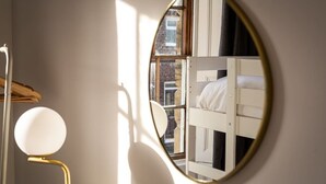 Een ronde spiegel met gouden lijst reflecteert een stapelbed en een raam.