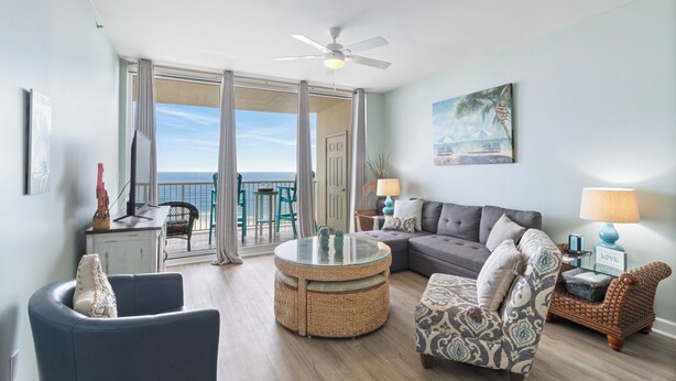 A spacious living room with a view of the ocean, a ceiling fan, and a comfortable seating area with a sofa and chairs.