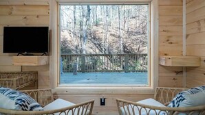 Habitación tipo cabaña con un ventanal grande, un televisor y dos sillones de mimbre.