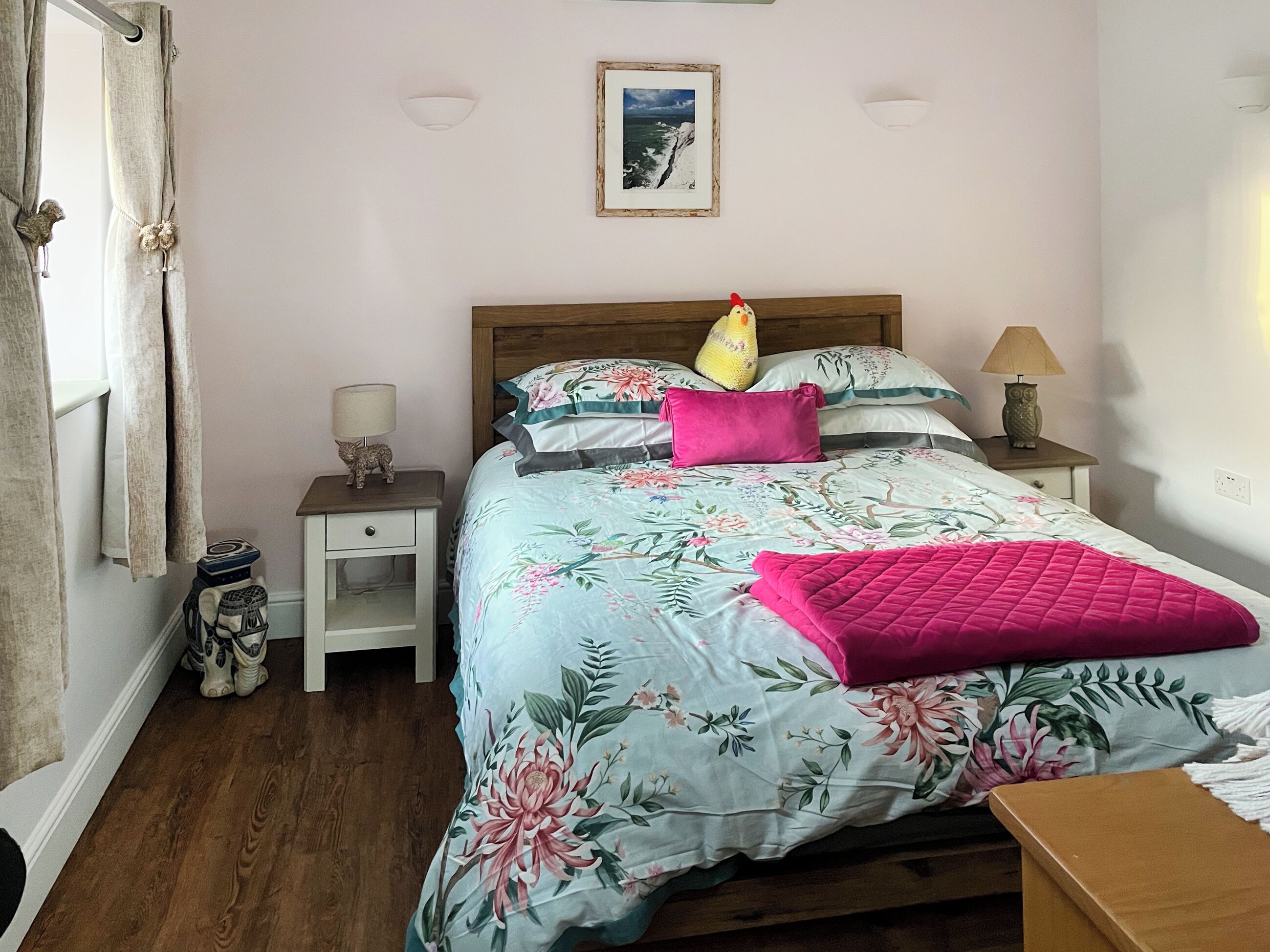 A bedroom with a bed, nightstands, a lamp, a picture on the wall, and a window with curtains.