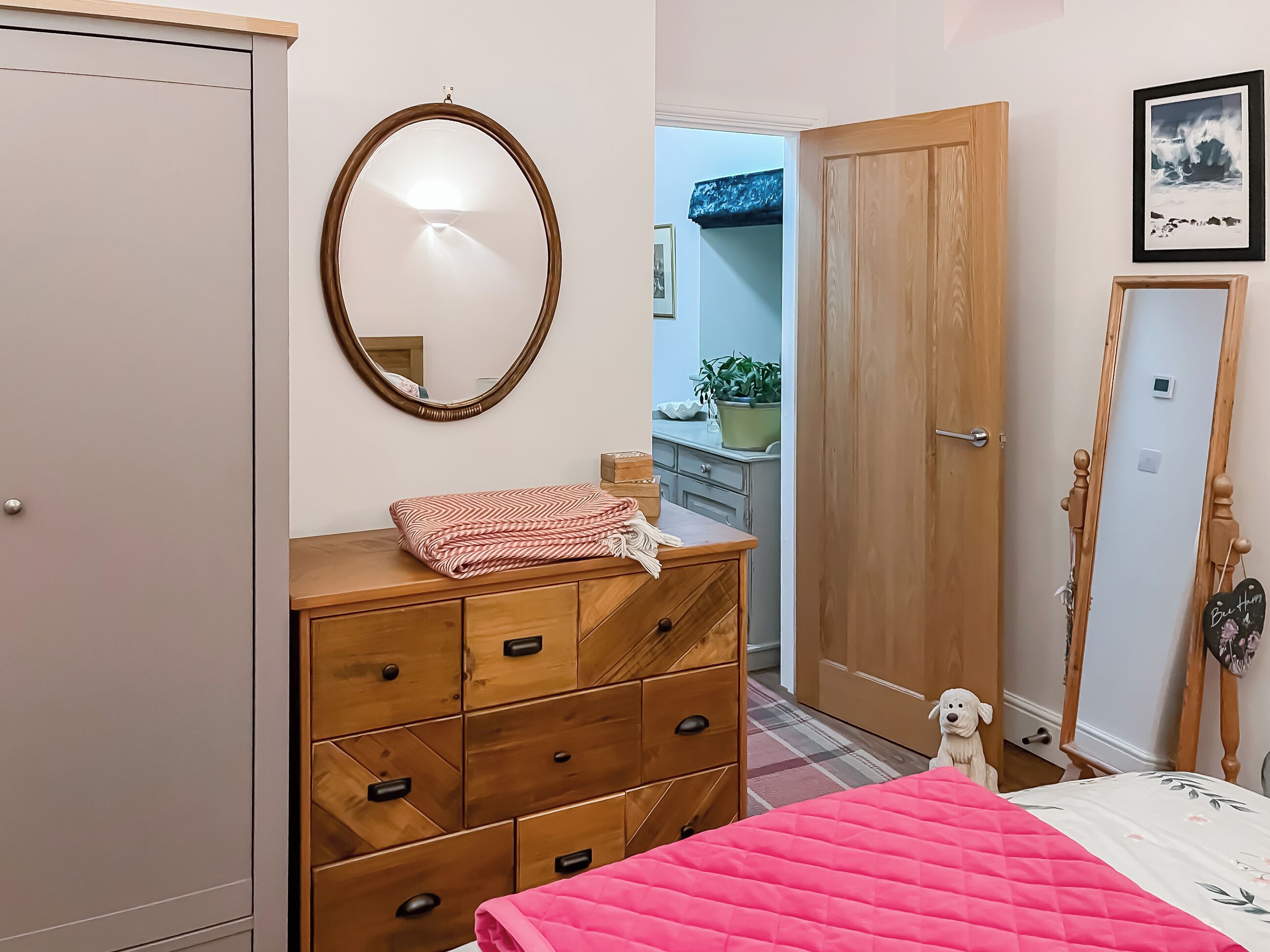 Una camera da letto con un letto, una cassettiera in legno, uno specchio e una porta.