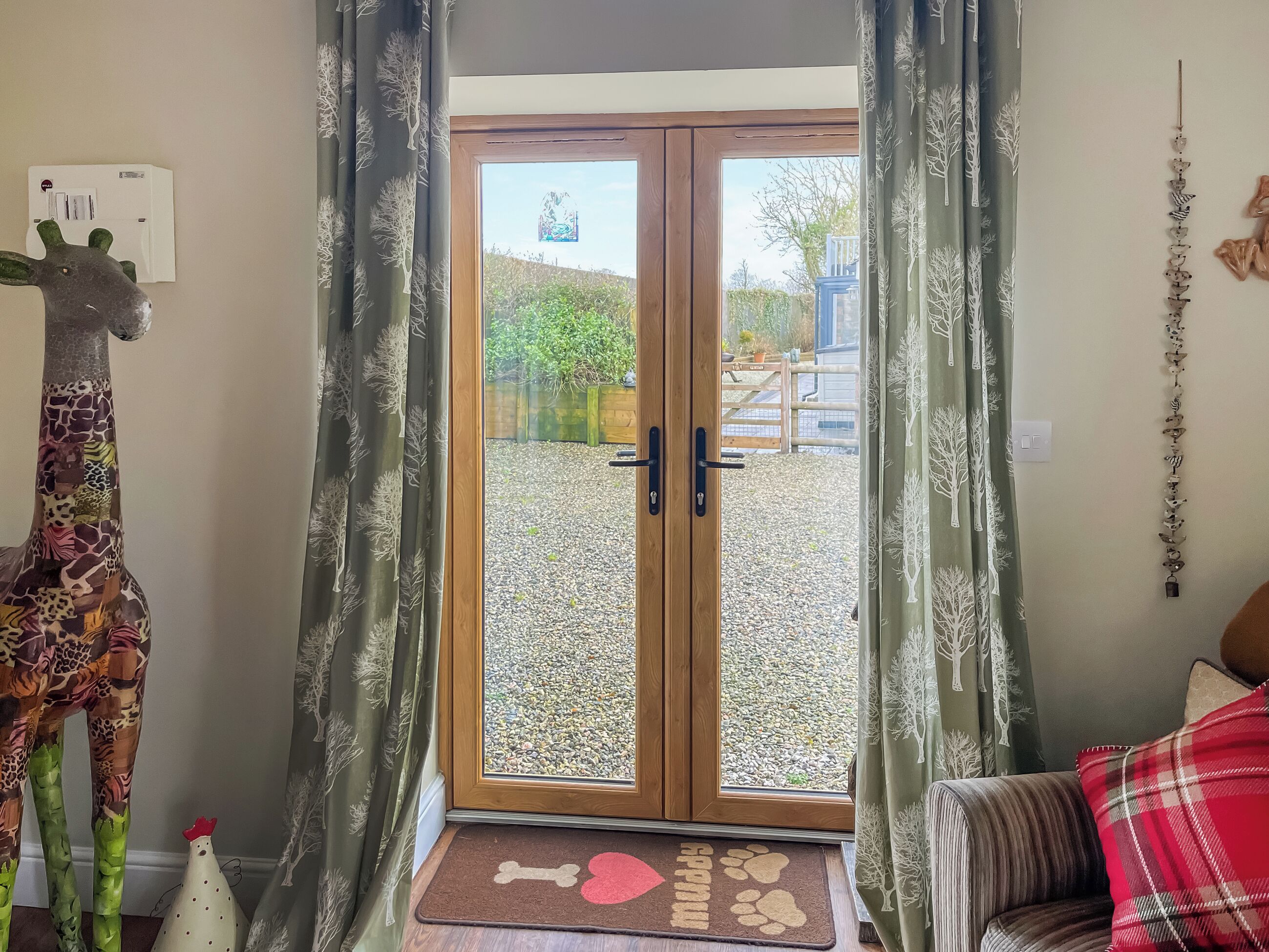 A room with a giraffe decoration, a wooden door, and a view of a gravel area outside.