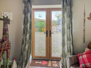 A room with a giraffe decoration, a wooden door, and a view of a gravel area outside.
