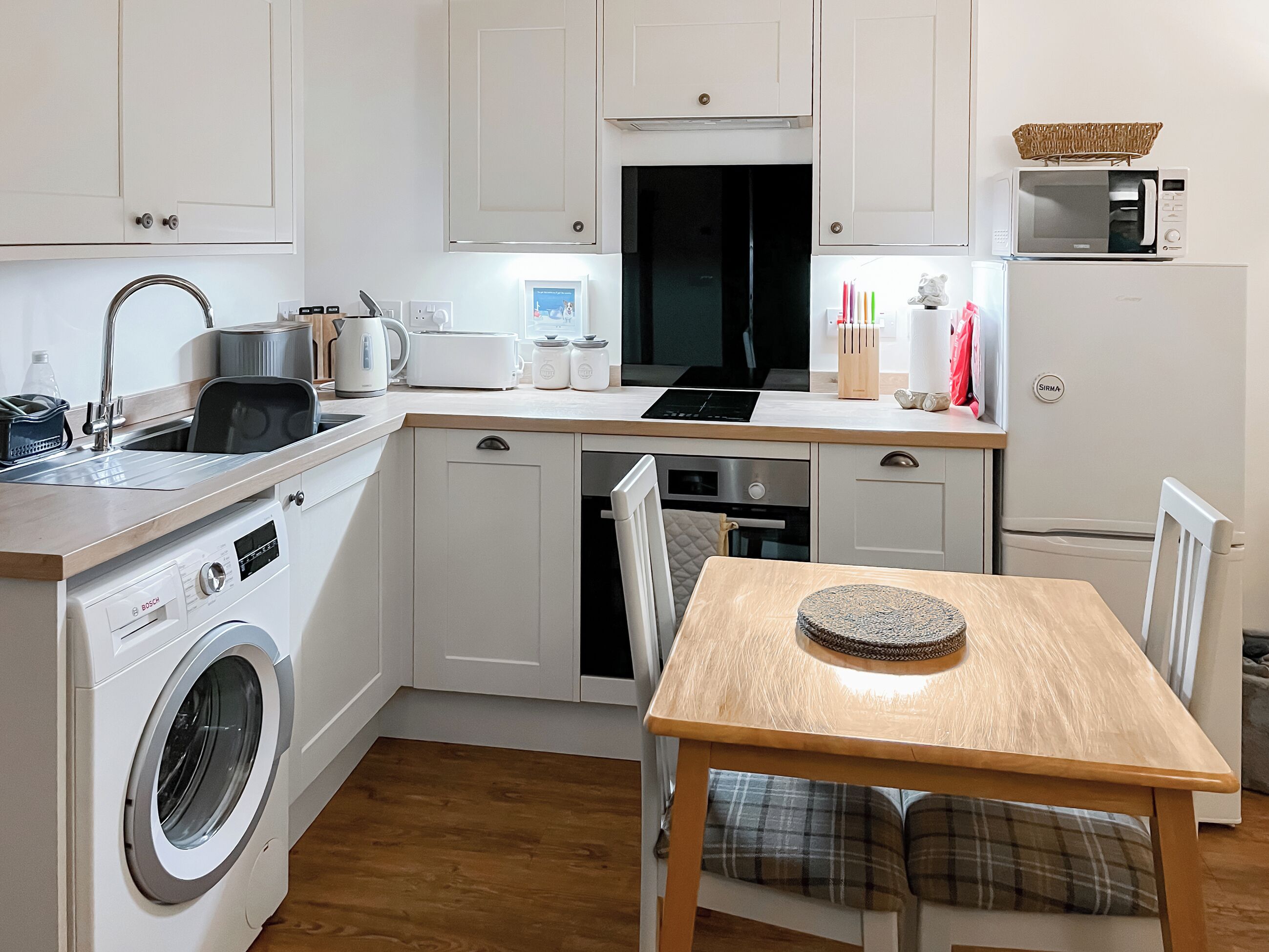 Cocina compacta con lavadora, microondas y comedor con mesa y sillas.