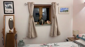 Un dormitorio con cama, ventana con cortinas, espejo y dos cuadros en la pared.