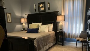 Un dormitorio ordenado con una cama grande, dos mesitas de noche con lámparas, una silla y un aparador.