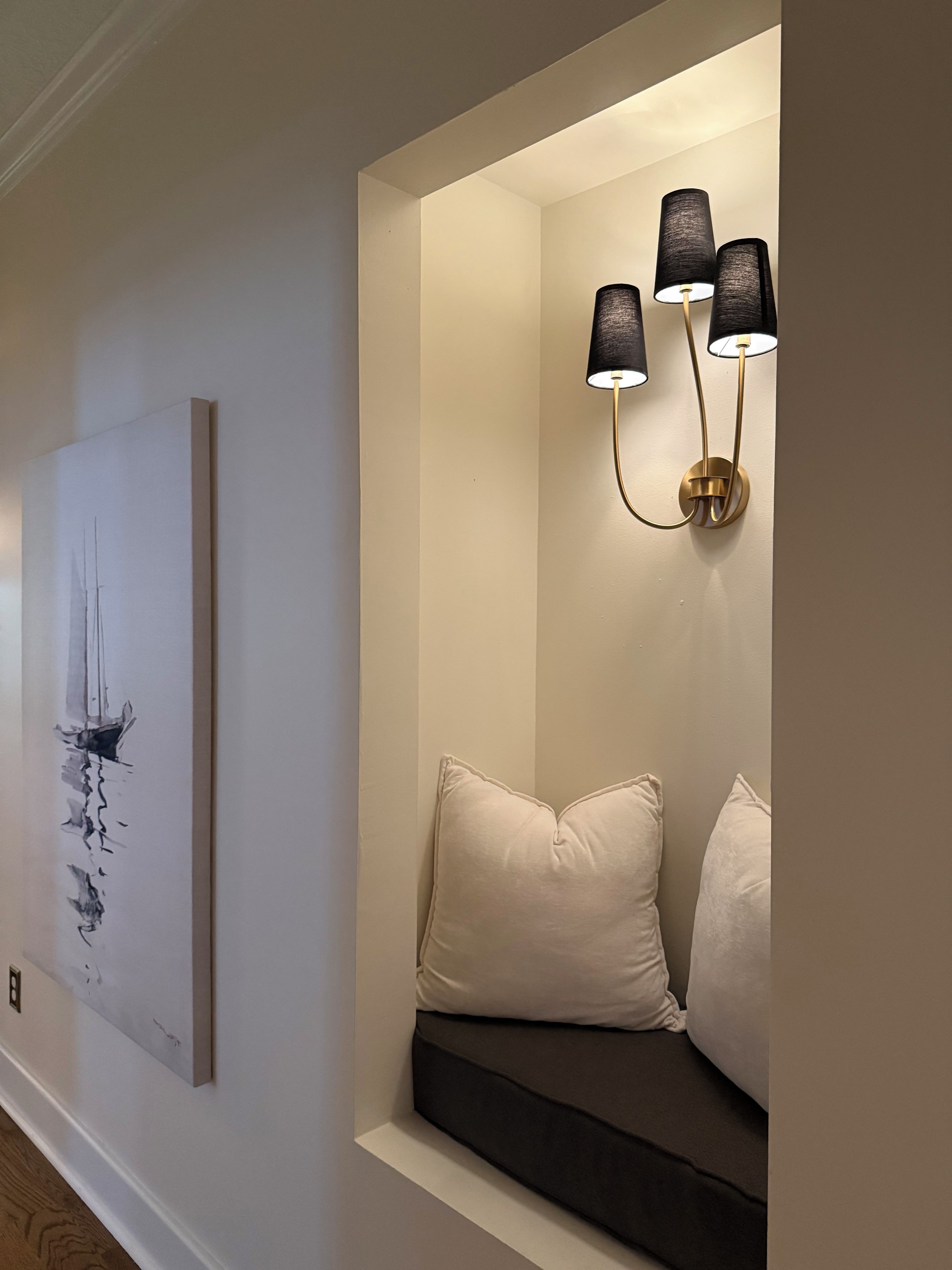 Ein modernes Interieur mit Wandbild, gepolstertem Sitzbänkchen mit Kissen und Wandleuchte.