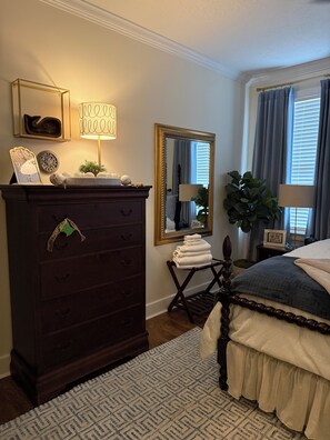 A bedroom with a dark wooden dresser, a bed with a white and blue patterned bedspread, a large mirror, and a window with curtains.
