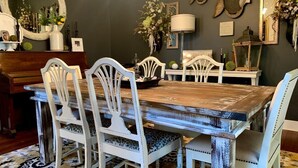 Un comedor con una mesa de madera rústica y sillas blancas, rodeado de decoración en las paredes y un espejo.