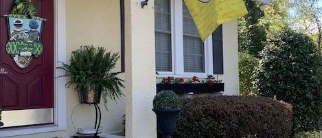Une maison avec une porte rouge, un drapeau jaune et un petit porche avec des marches menant à l’entrée.